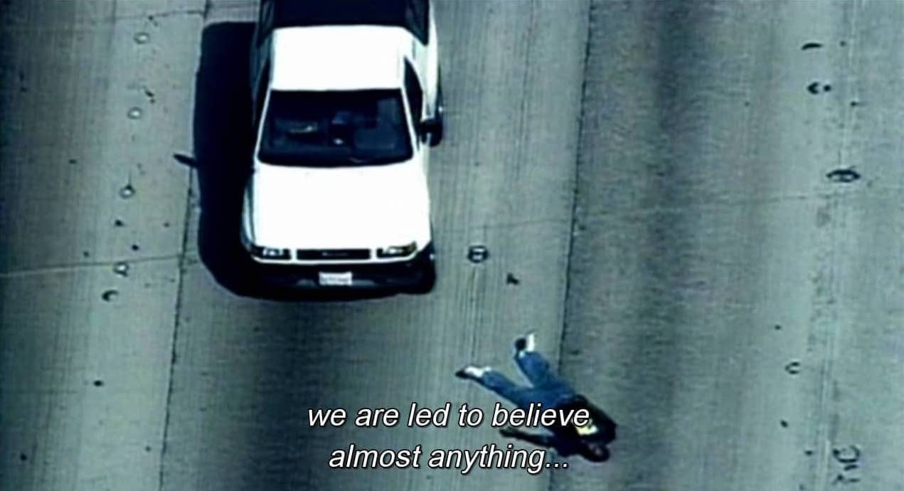 Tela de TV mostra carro em autoestrada e corpo ao lado, com os dizeres We are led to believe almost anything...